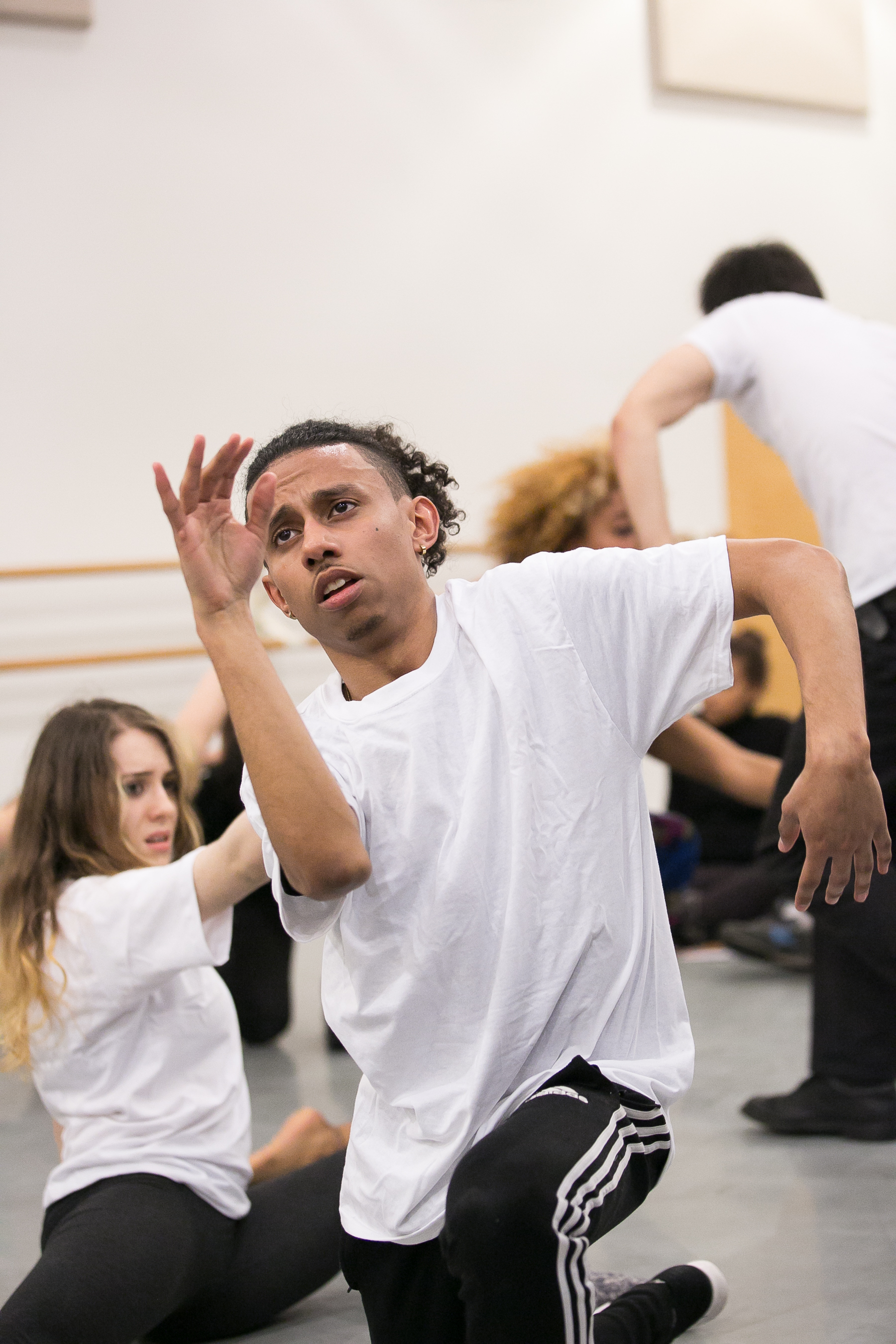 SharedSpace Image description: Dancer is down on one knee with their right hand in front of their face and their left elbow lifted and out to the side. They emote a passionate face as they gaze at their front hand. Another dancer is to their right sitting in a twisted shape on the floor.