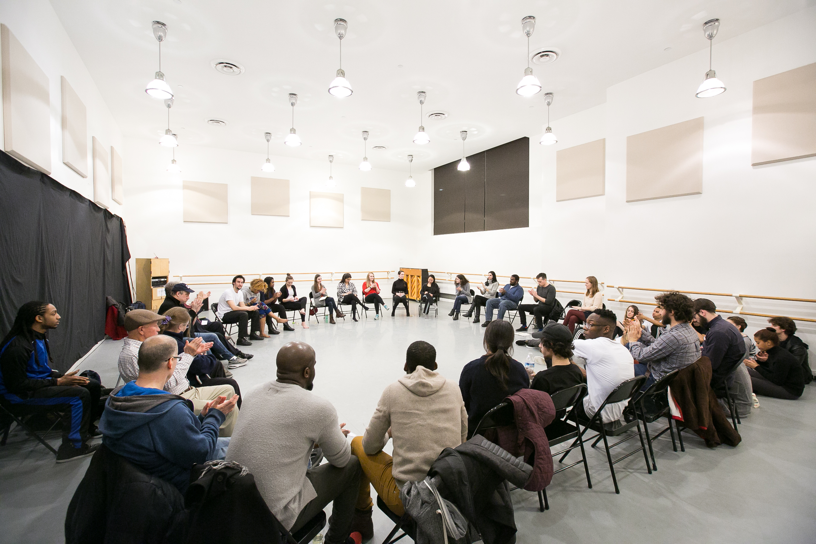 Shared Space Image description: A group of people seated in chairs in a large circle that fills up the entire dance studio.