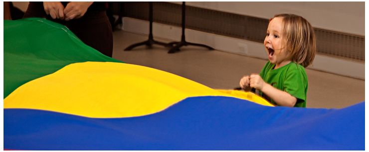 Toddler with big happy expression holding the handle of parachute.
