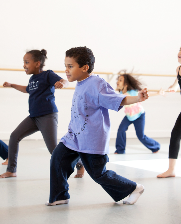 Image description: Side profile of a young boy wearing a lavender shirt in a high lunge position with his arms out to the side.