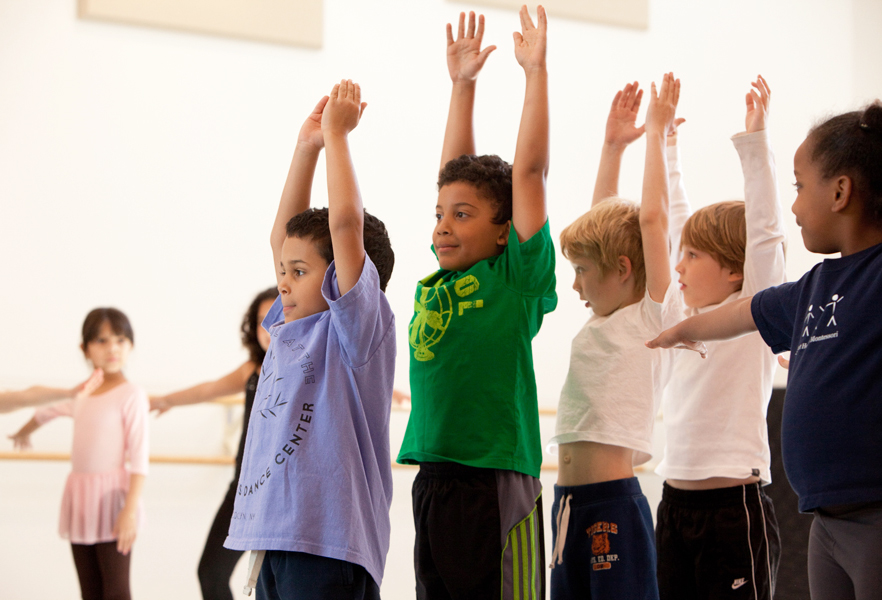 Image description: Line of students with their arms reaching up to the sky.