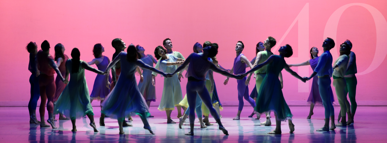 The Mark Morris Dance Group in "L'Allegro." They are standing in a circle in front of a bright pink background. Hidden in the top right corner is "40" in a light pink color.