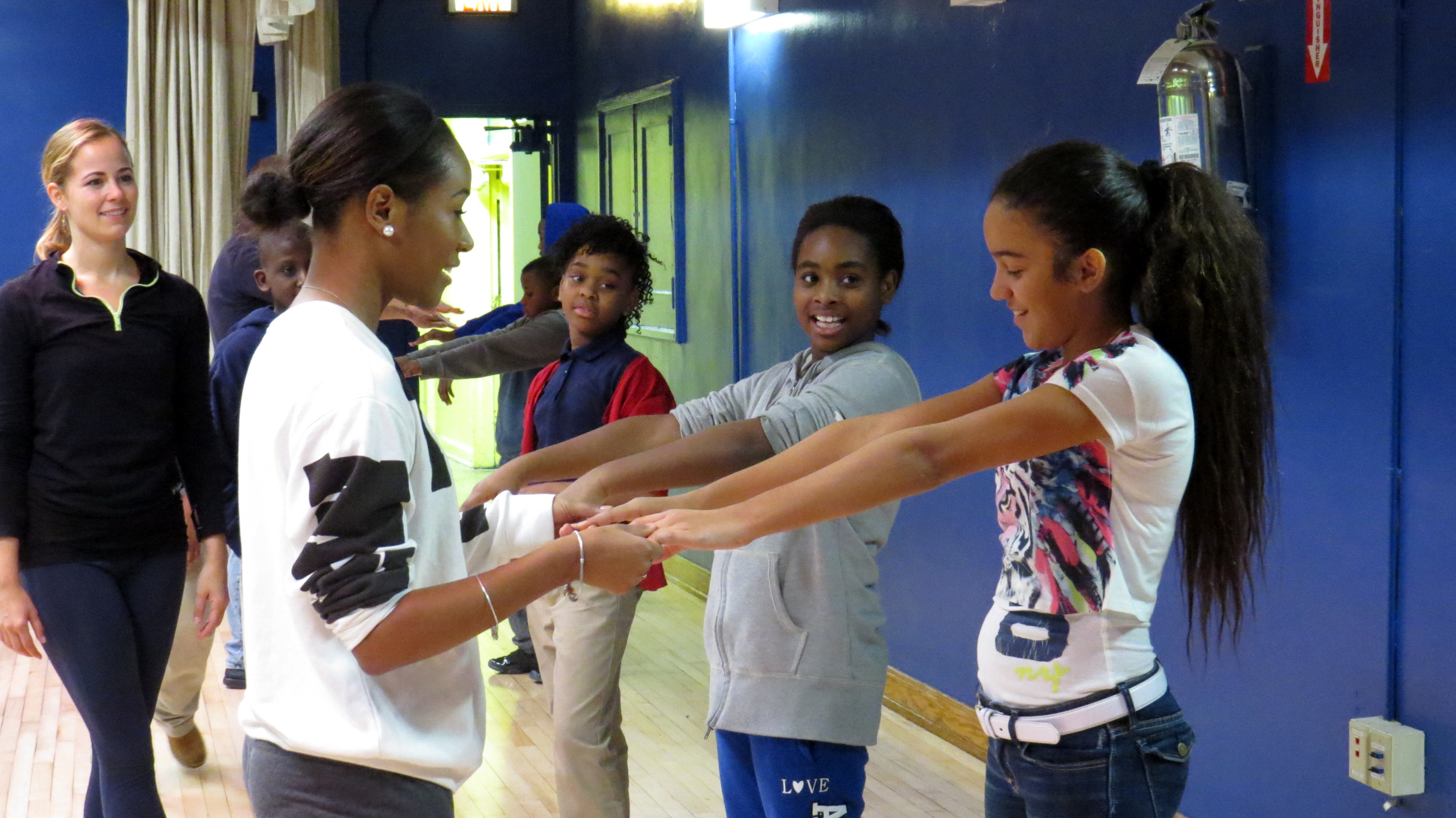 A line of students are standing on one side with their arms stretched forward. Another student is facing the student who is at the front of the line and is holding their hands.