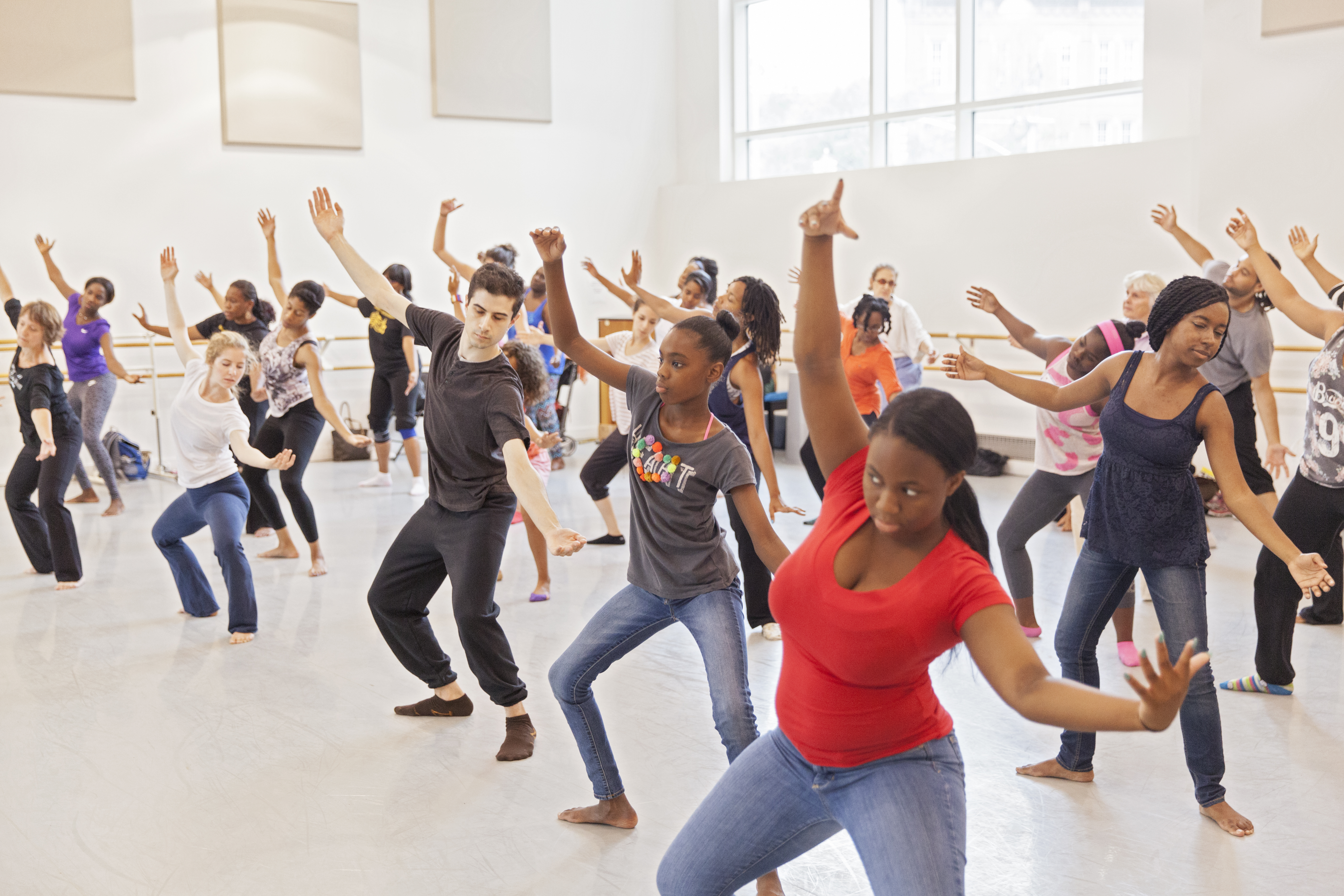 Dancers in a side arch with arms open, taking class in a dance studio.